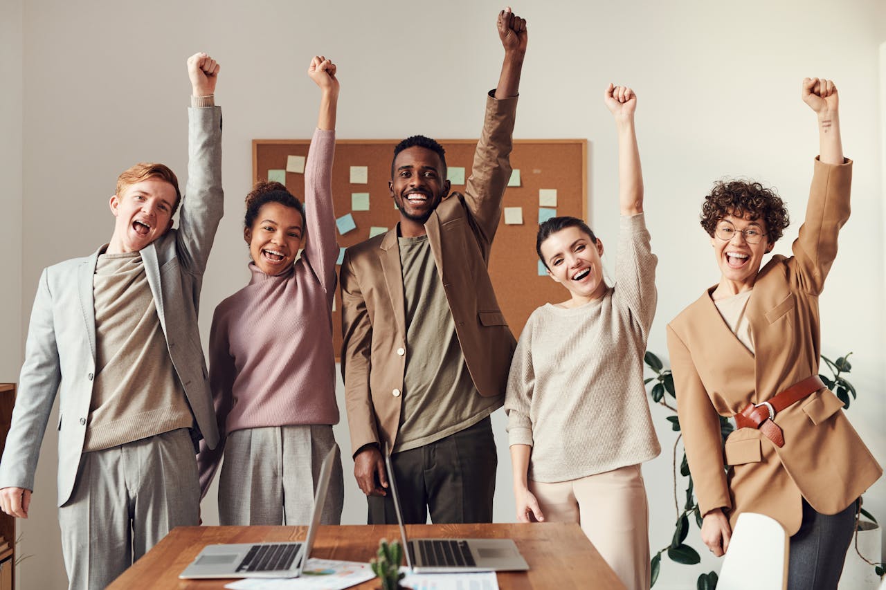 services-03 A diverse team celebrating success with raised hands in a modern office setting.