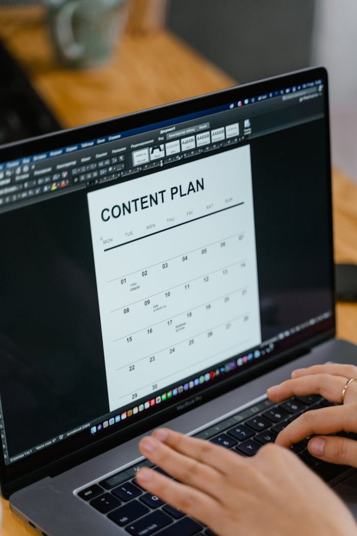about-bg Close-up of hands typing on a laptop displaying a content plan document, ideal for business or marketing content.
